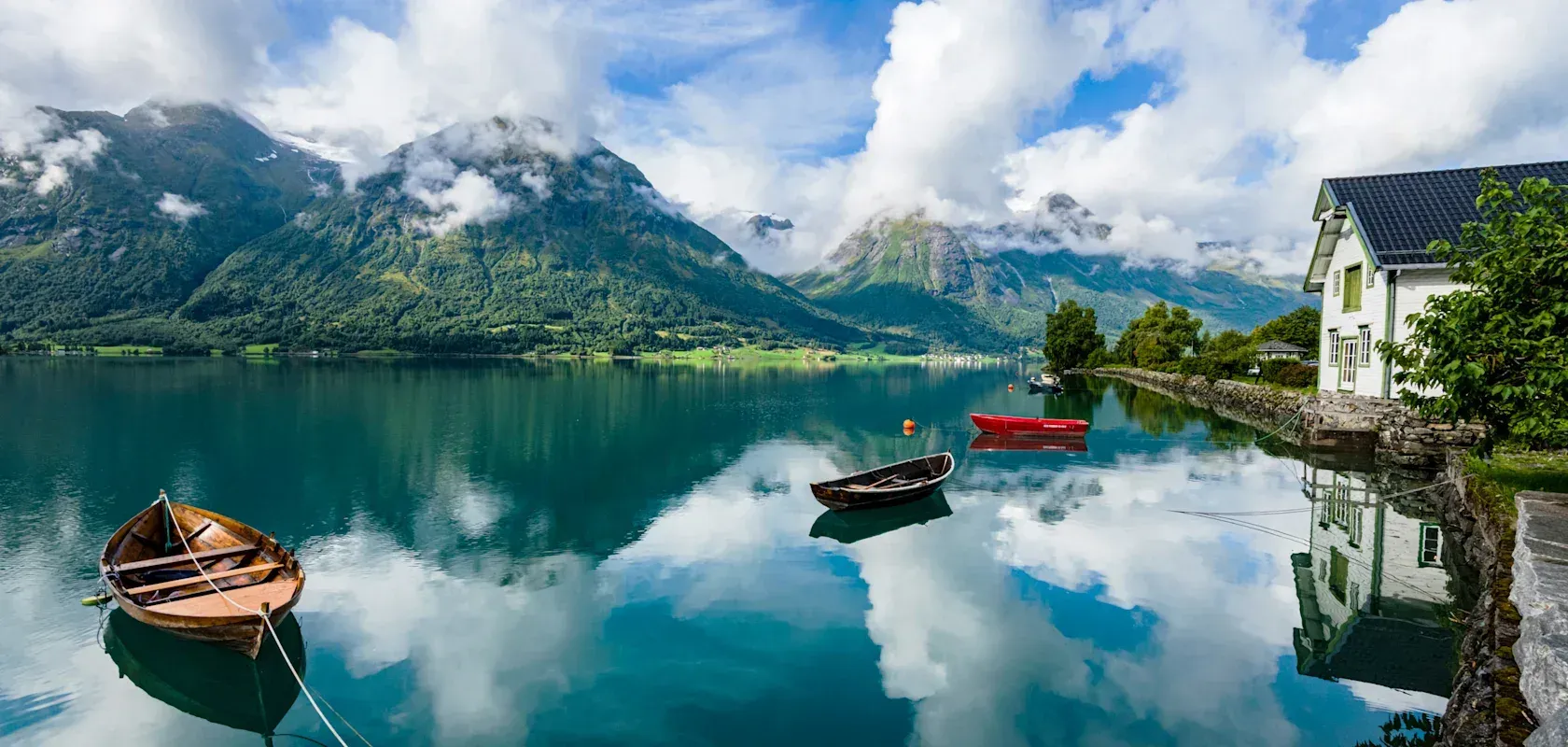Wooden rowing boats on a still Norwegian fjord, with mountains and low cloud reflected in the water