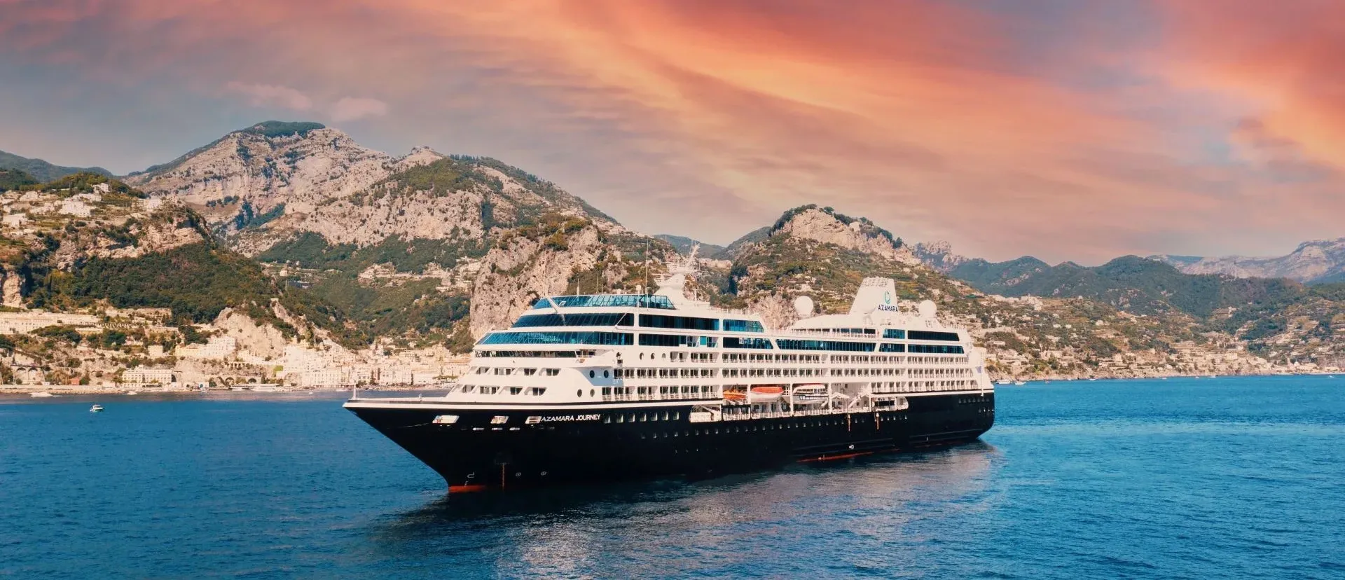 An Azamara ship at anchor off the Amalfi Coast at sunset, with hillside villages behind