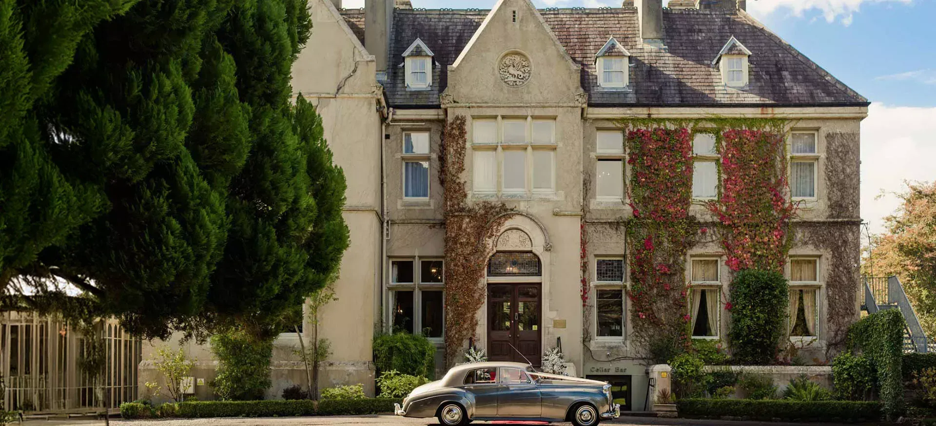 A vintage car parked outside an ivy-covered country house hotel, the kind of stay Back-Roads Touring uses