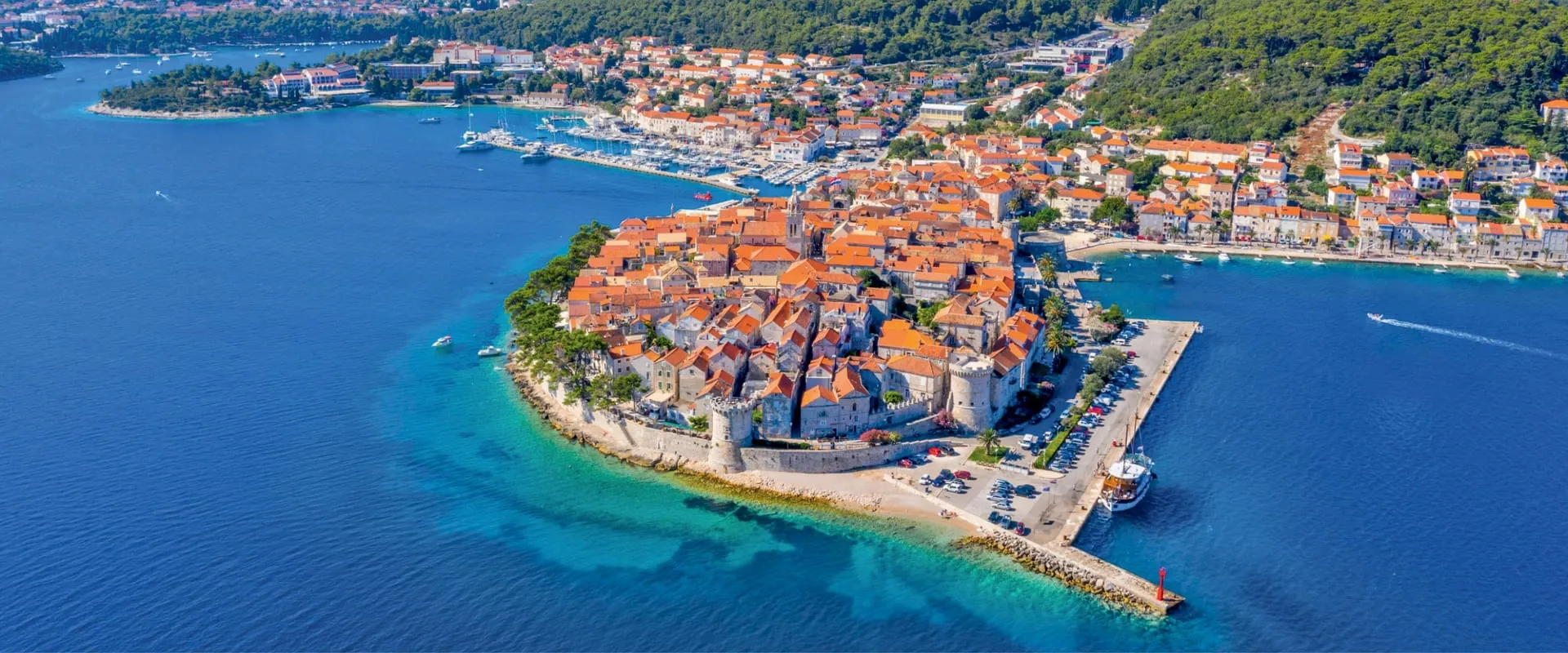 Aerial view of Korcula's fortified old town on a narrow Dalmatian peninsula in Croatia, surrounded by turquoise water, with terracotta rooftops and a small marina