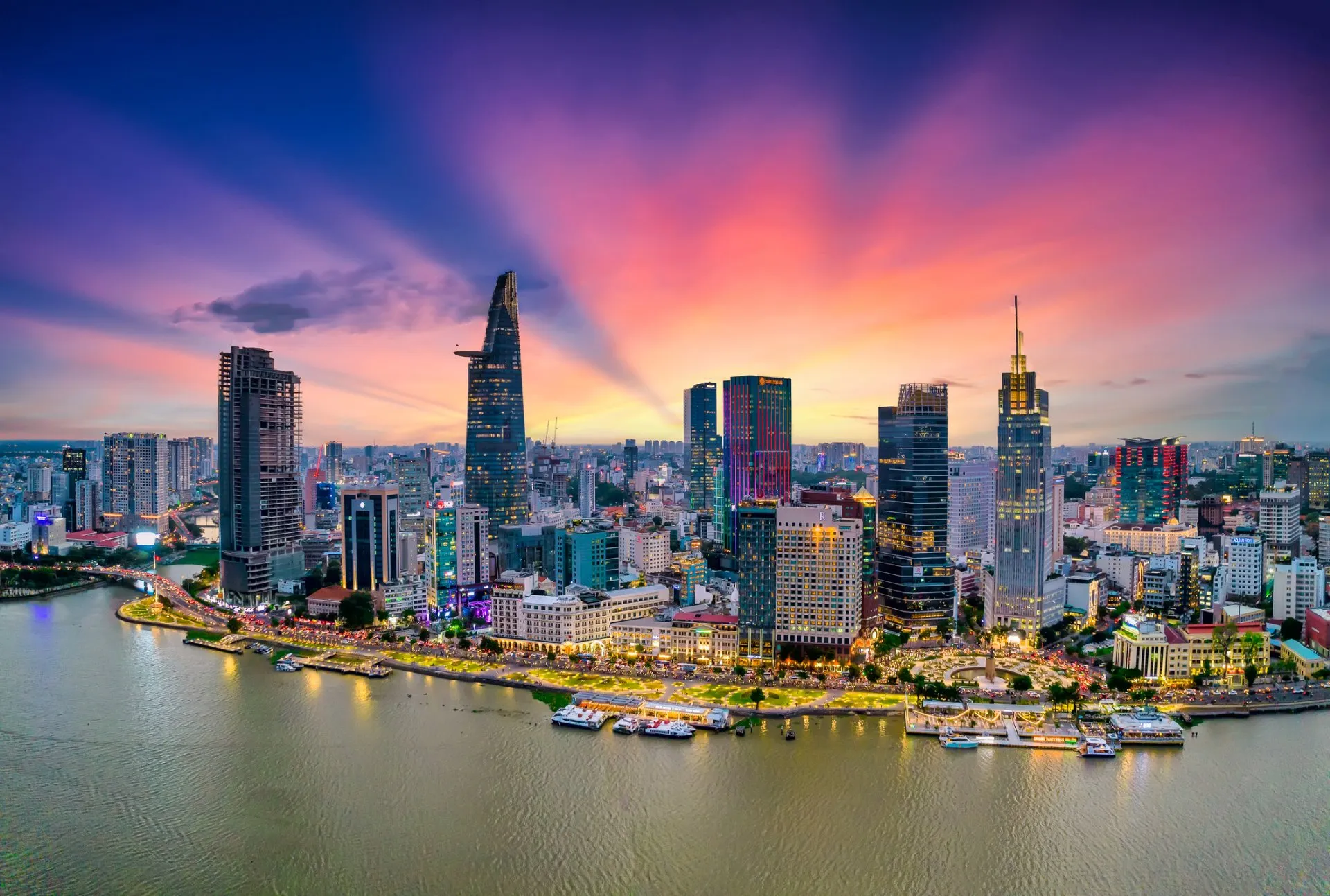 Aerial view of Ho Chi Minh City's skyline at dusk, with the Landmark 81 skyscraper rising above the Saigon River lined with illuminated boats and barges