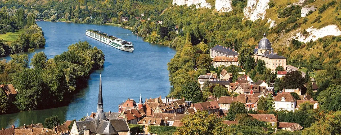 A Scenic river ship on the Seine passing the village of Les Andelys, with its church spire, château and the chalk cliffs of Normandy behind